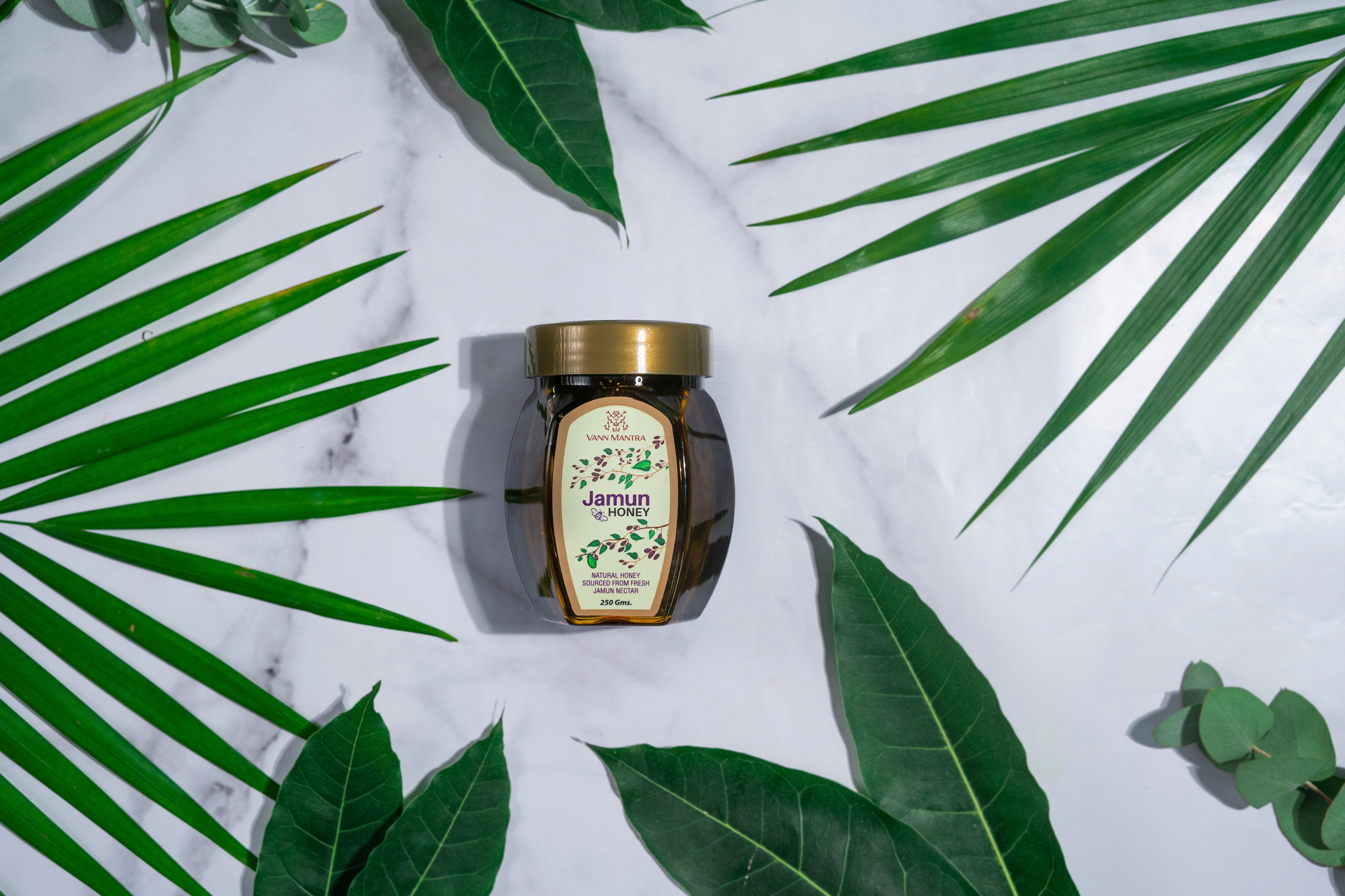 Jar of Jamun Honey on a backdrop with plants. 