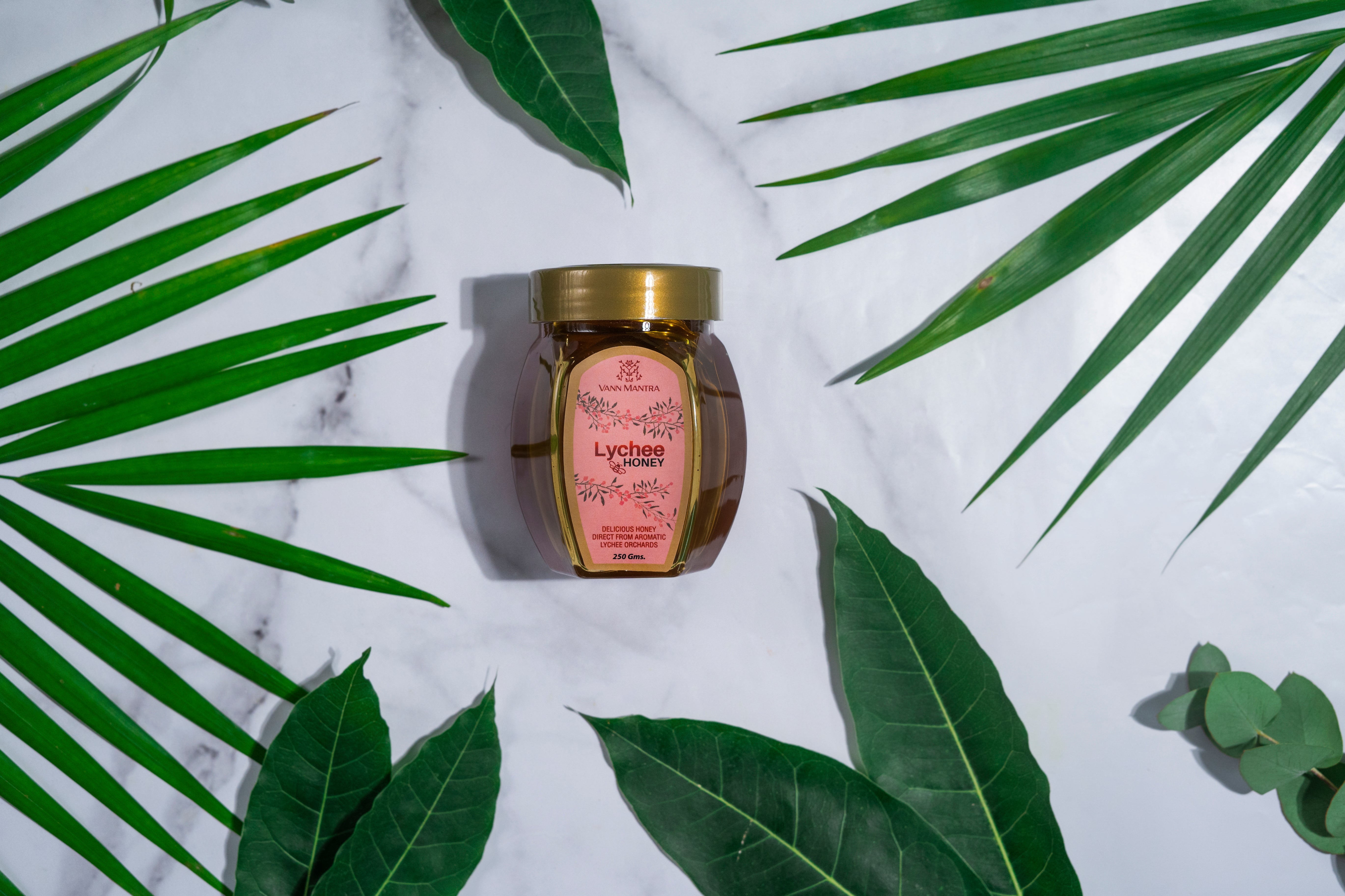 Jar of Lychee Honey on a backdrop with plants. 