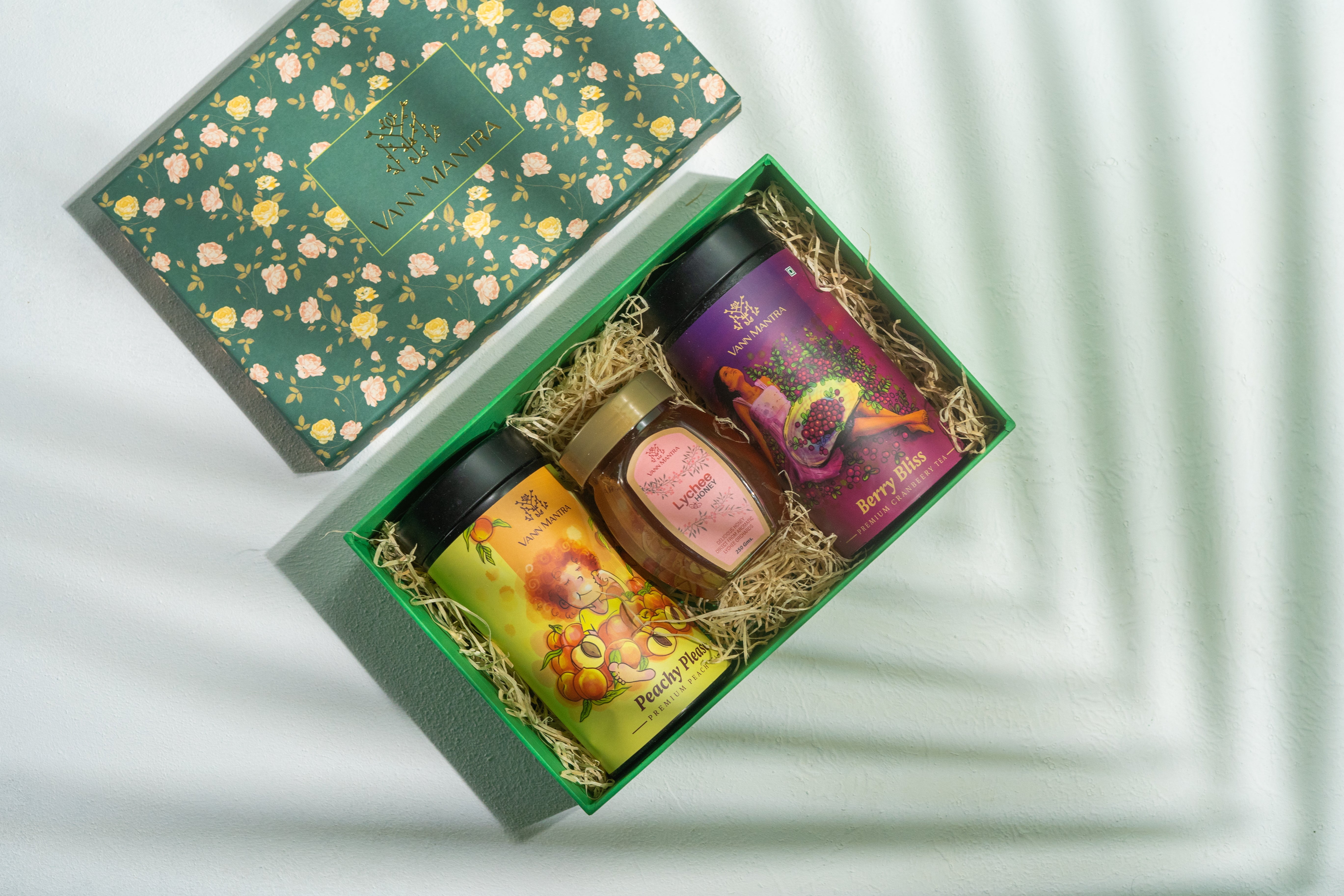 Box Of Satisfaction (Peachy Please, Berry Bliss, Lychee Honey) on a backdrop with plants