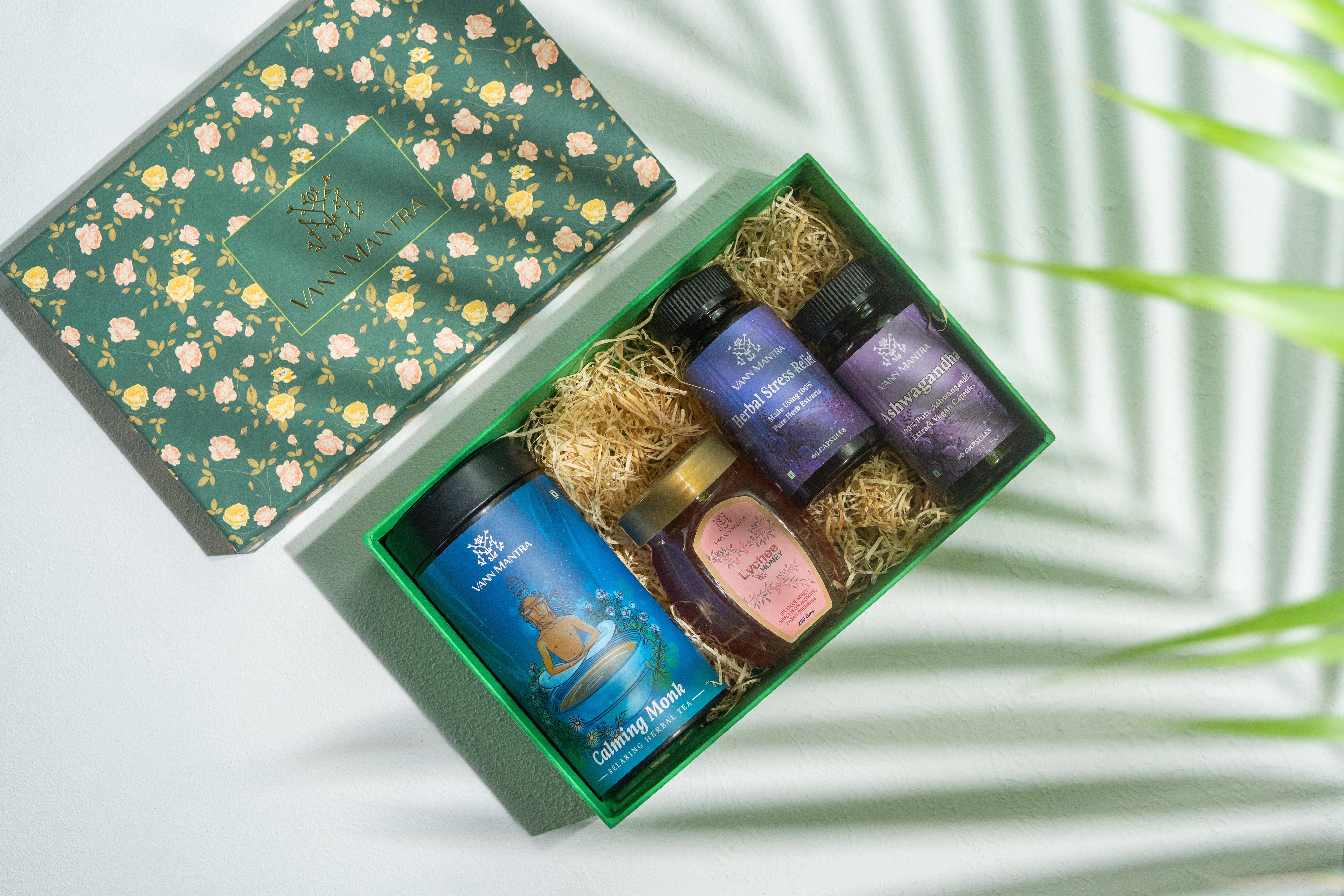 Box Of Inner Peace ( Calming Monk Tea, Herbal Stress Relief Capsule, Ashwagandha Capsules & Lychee Honey) on a backdrop with plants