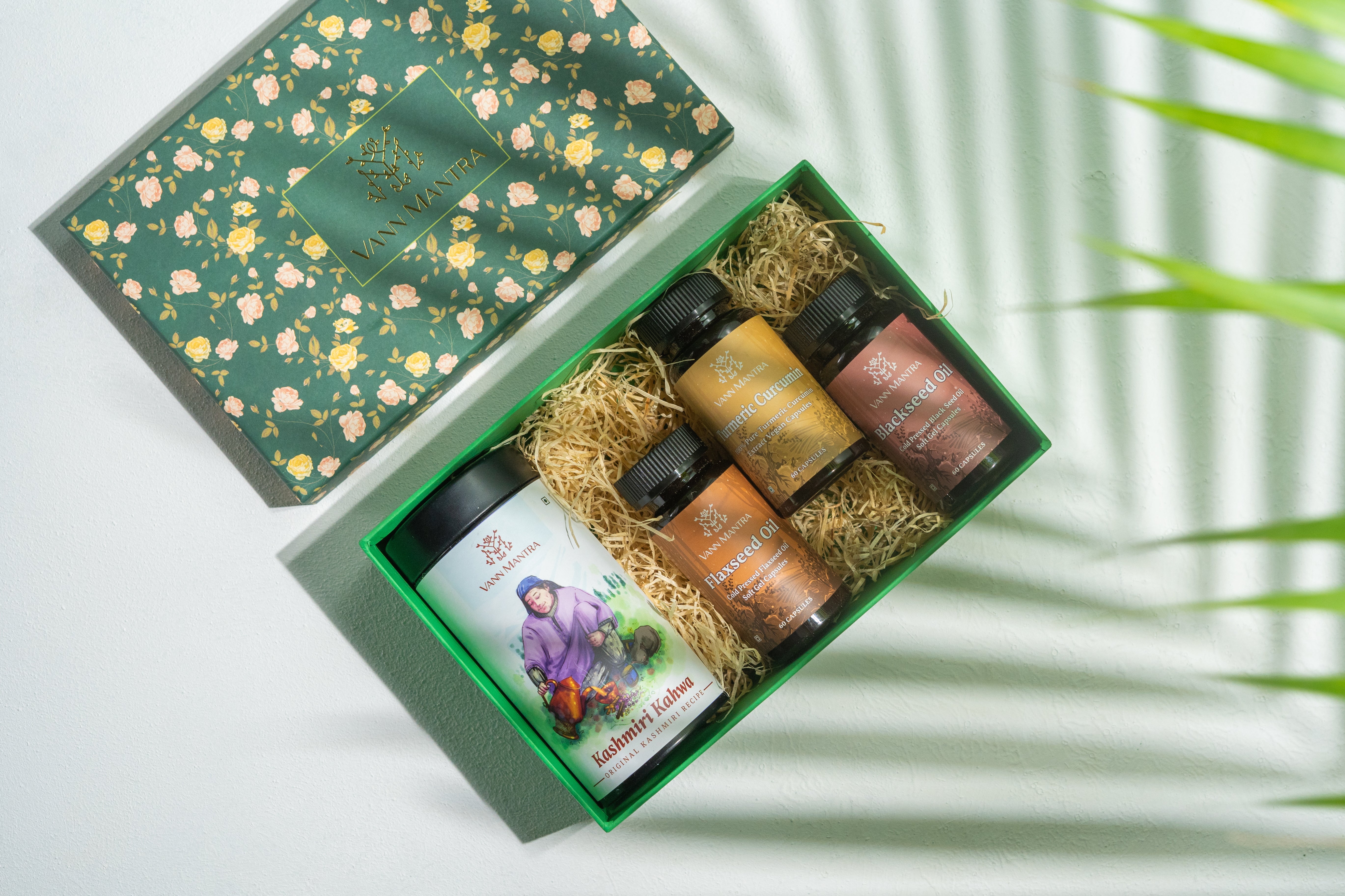 Box Of Grandma's Immunity Secrets ( Kashmiri Kahwa, Flaxseed Oil Capsule, Blackseed Oil Capsule, Turmeric Curcumin Capsule) on a backdrop with plants.