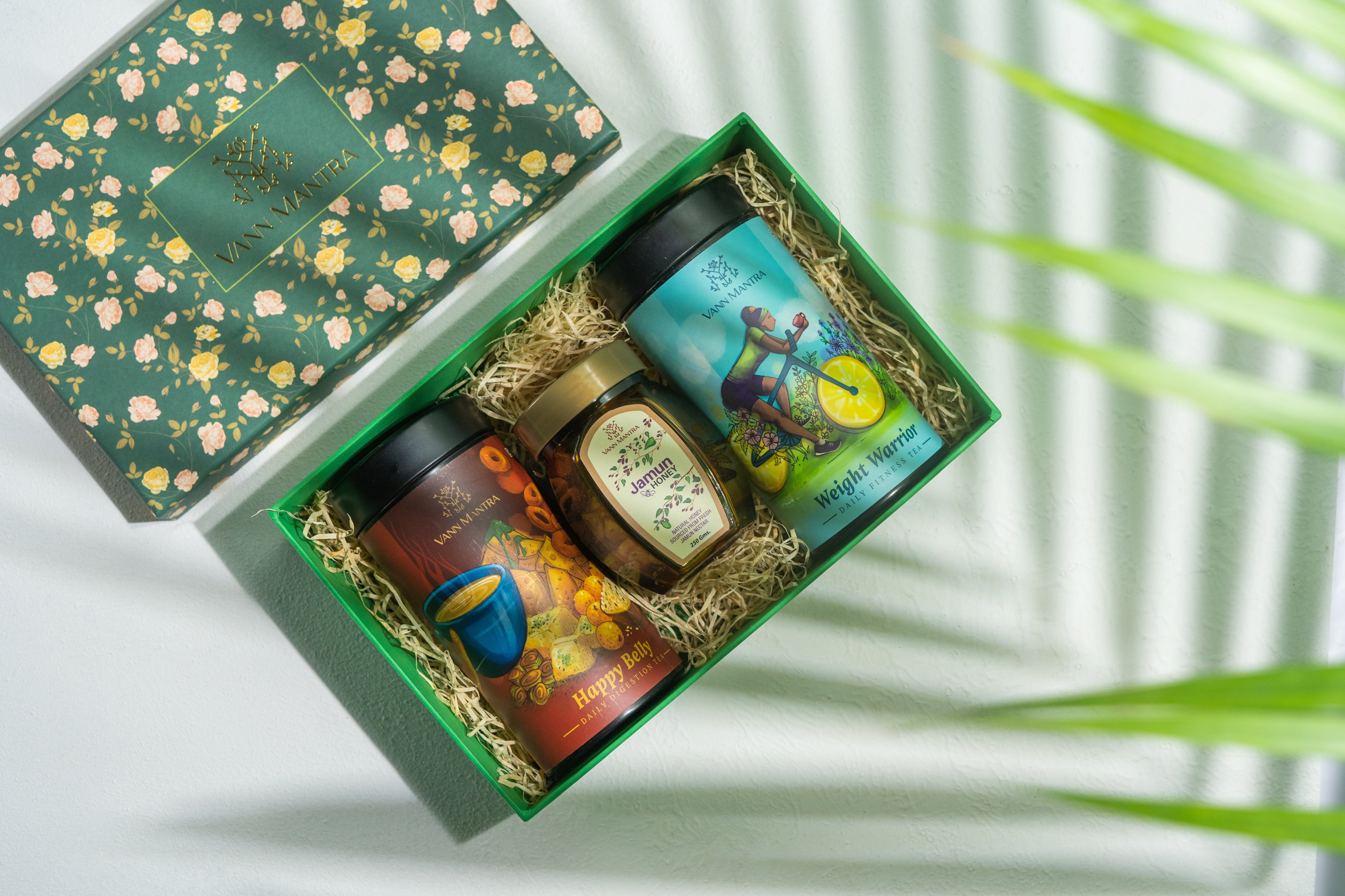Box Of Vitality (Happy Belly, Weight Warrior, Jamun Honey) on a backdrop with plants